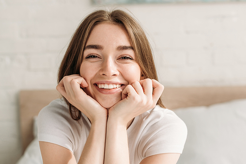 cheerful young woman laughing at camera while holding hands near face