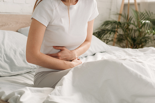 cropped view of woman sitting in bed and suffering from stomach pain