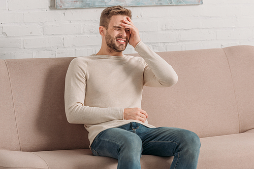 frowned man sitting on sofa with closed eyes while suffering from headache