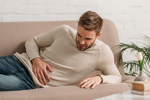 young man lying on sofa and suffering from abdominal pain