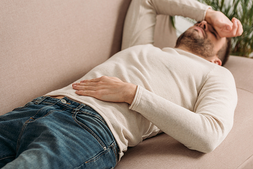 selective focus of man lying on sofa and suffering from headache