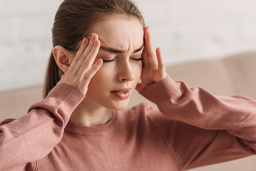 young woman holding hands near head while suffering from migraine with closed eyes