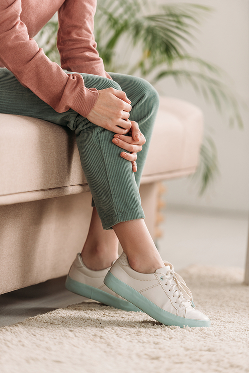 cropped view of woman sitting on sofa and suffering from knee pain