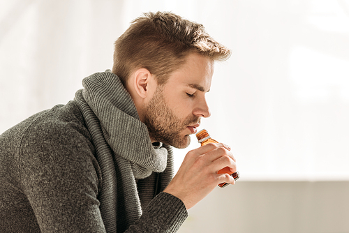 sick man in warm scarf drinking cough syrup with closed eyes