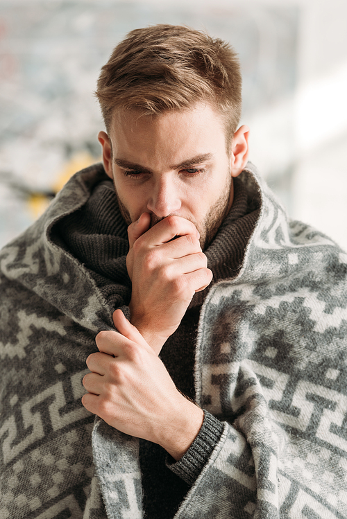 sick man, wrapped in blanket, coughing while covering mouth with hand