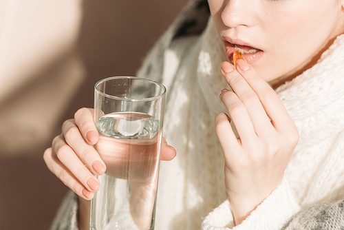 cropped view of sick woman holding glass of water while taking medicine