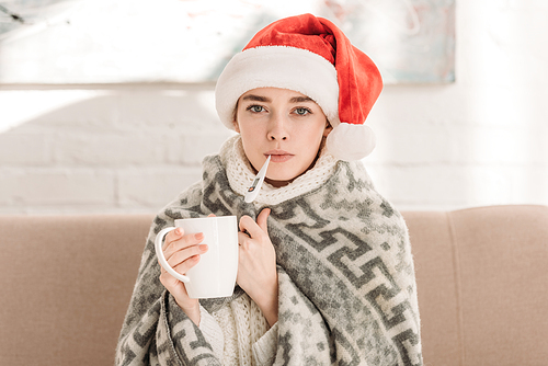 sick girl in santa hat, wrapped in blanket,  and holding cup of tea