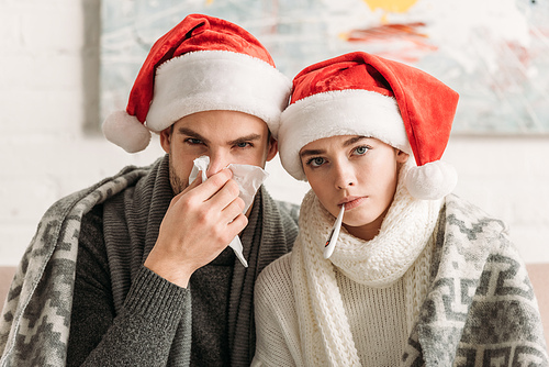 diseased couple wearing santa hats and covered with blanket 