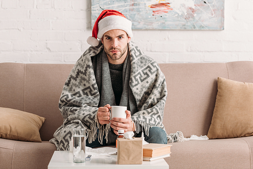 sick man in santa hat  while holding cup of warm drink
