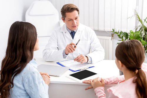 serious ent physician talking to mother and daughter near digital tablet with blank screen on desk