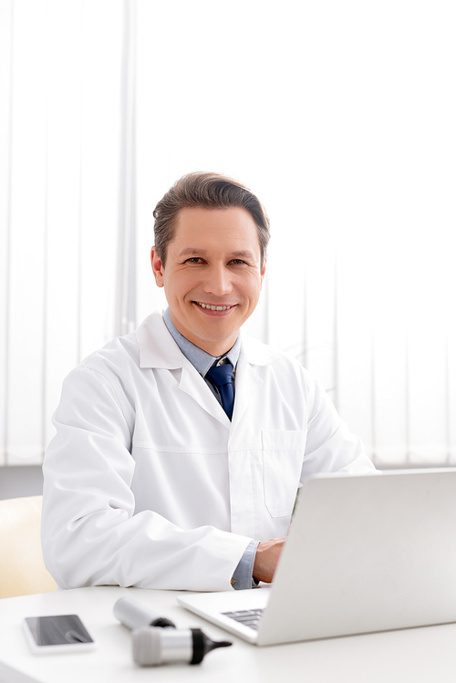 smiling otolaryngologist  while using laptop at workplace