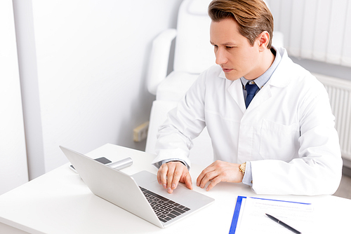 attentive ent physician using laptop while sitting at workplace
