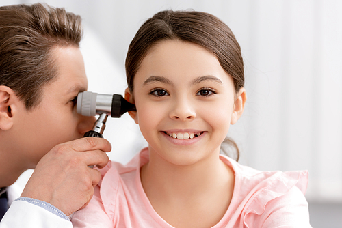 ent physician examining ear of cheerful kid with otoscope