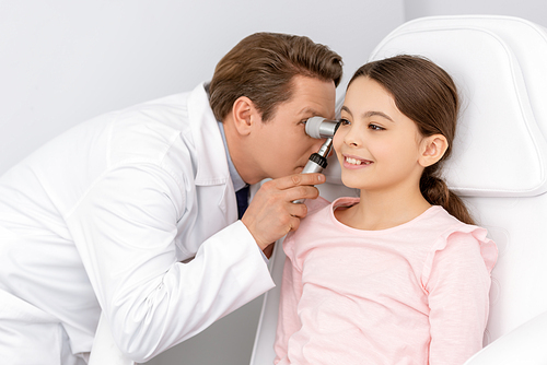 attentive ent physician examining ear of smiling kid with otoscope