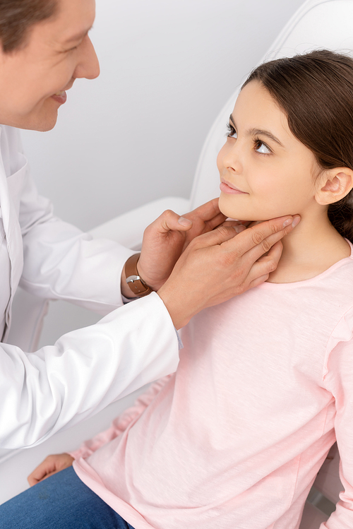 smiling ent physician touching neck of cute child while examining her throat