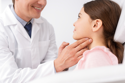 cropped view of smiling ent physician touching neck of cute child while examining her throat