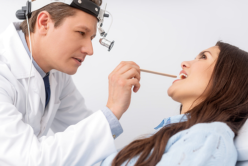 attentive otolaryngologist in ent headlight examining throat ao attractive patient with throat spatula