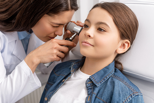 attentive otolaryngologist examining ear of adorable smiling child with otoscope