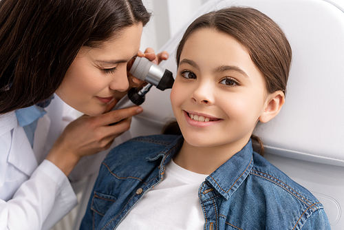 attentive otolaryngologist examining ear of smiling child with otoscope