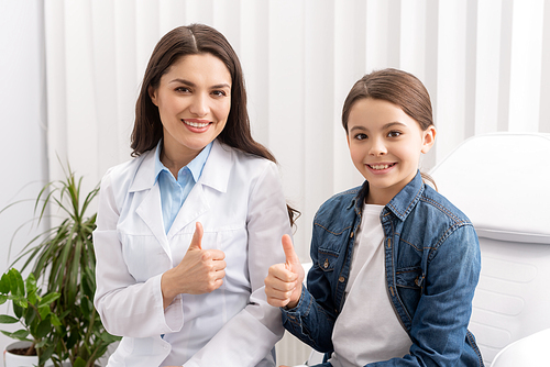happy ent physician and child showing thumbs up while smiling at camera