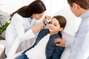 cropped view of father touching shoulder of daughter sitting in medical chair while otolaryngologist examining her ear with otoscope