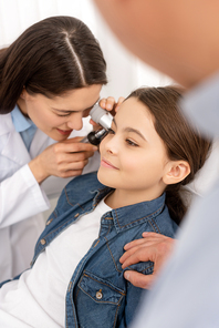 cropped view of father touching shoulder of daughter while otolaryngologist examining her ear with otoscope