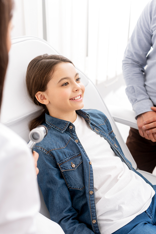 selective focus of smiling child near father and ent physician with otoscope