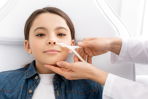 cropped view of otolaryngologist examining nose of kid with nasal speculum