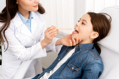 partial view of otolaryngologist examining throat of kid with tongue depressor
