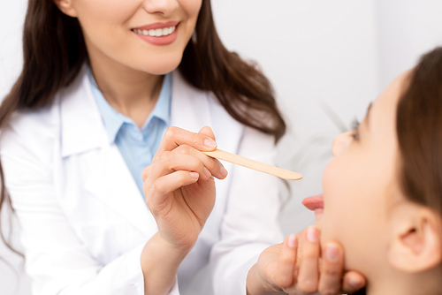 cropped view of ent physician examining throat of kid with tongue depressor