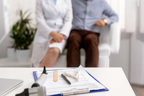 selective focus of desk with ent diagnostic equipment on clipboard, and otolaryngologist with patient sitting on background