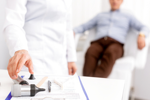 selective focus of ent physician taking otoscope and patient sitting in medical chair on background