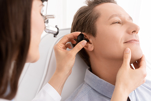 cropped view of otolaryngologist in ent headlight examining ear of handsome patient