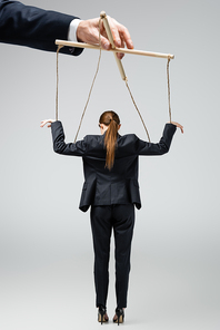 cropped view of puppeteer holding businesswoman marionette on strings isolated on grey