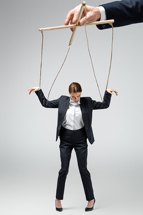 cropped view of puppeteer holding businesswoman marionette on strings isolated on grey