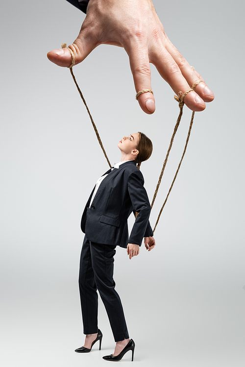 cropped view of puppeteer holding businesswoman marionette on strings isolated on grey