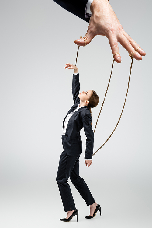 cropped view of puppeteer holding businesswoman marionette on strings isolated on grey