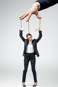 cropped view of puppeteer holding businesswoman marionette on strings isolated on grey
