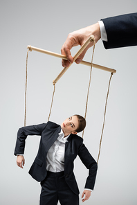 cropped view of puppeteer holding businesswoman marionette on strings isolated on grey