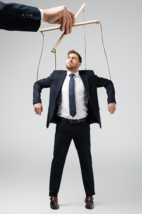 cropped view of puppeteer holding businessman marionette on strings isolated on grey