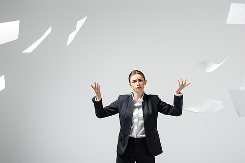 displeased businesswoman in suit throwing papers in air isolated on grey