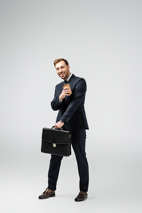 happy businessman with leather suitcase and paper cup isolated on grey
