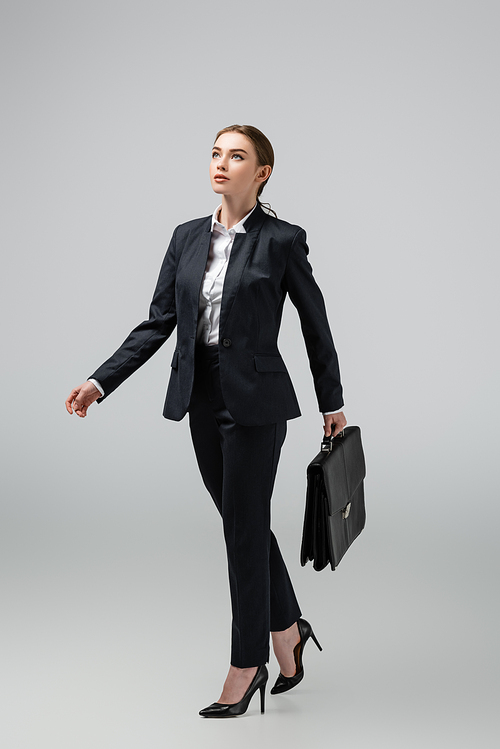 young businesswoman walking with leather suitcase isolated on grey