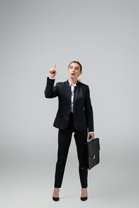 young businesswoman with leather suitcase pointing up isolated on grey