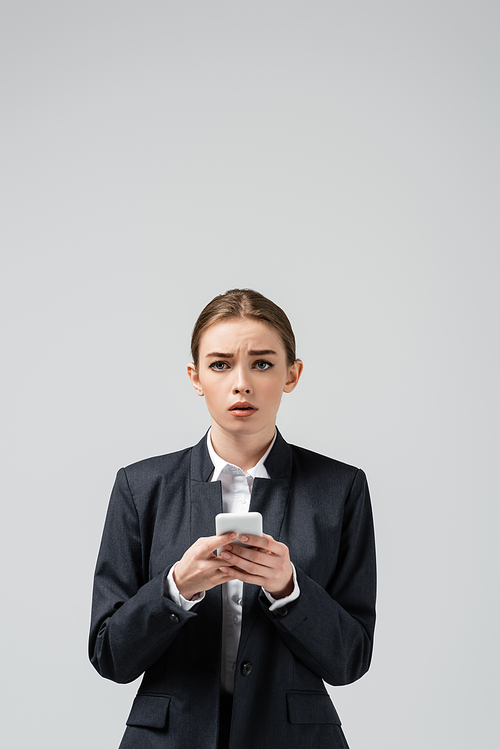 sad young businesswoman using smartphone isolated on grey