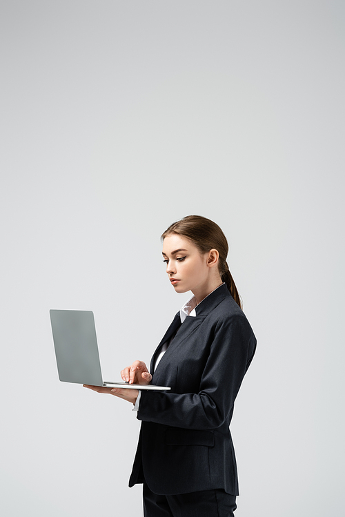 serious young businesswoman using laptop isolated on grey