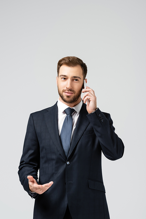 handsome businessman in suit talking on smartphone isolated on grey