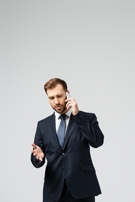confused handsome businessman in suit talking on smartphone isolated on grey