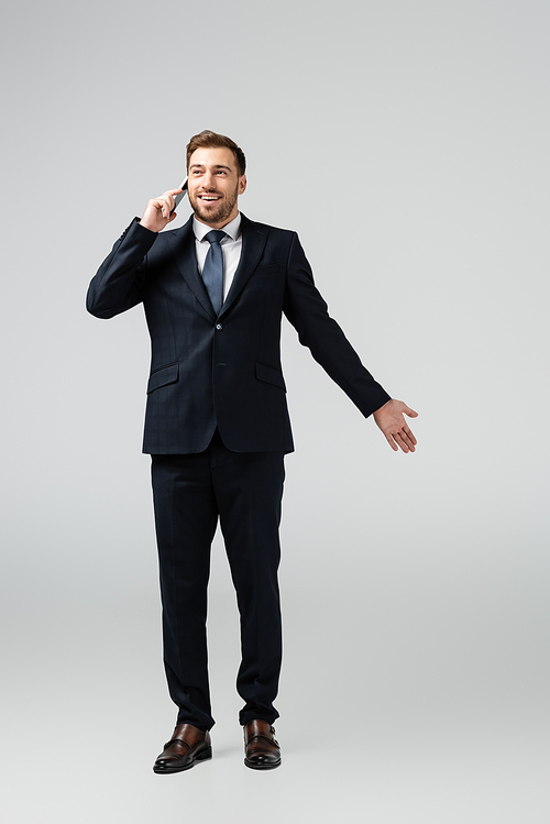 smiling handsome businessman in suit talking on smartphone isolated on grey