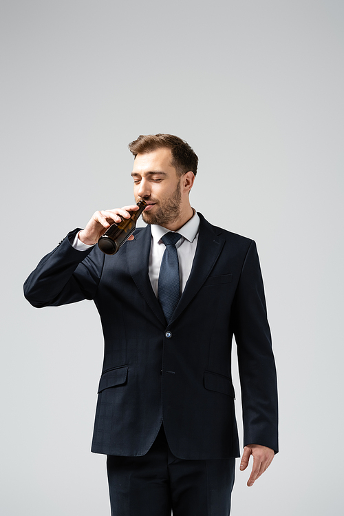 handsome businessman in suit drinking beer isolated on grey